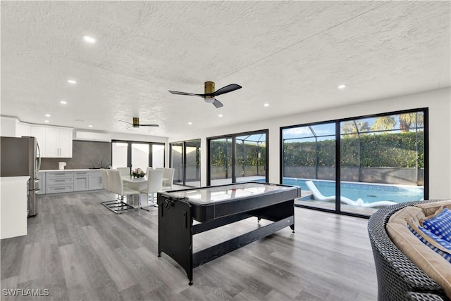 living room with ceiling fan, sink, plenty of natural light, a textured ceiling, and light wood-type flooring