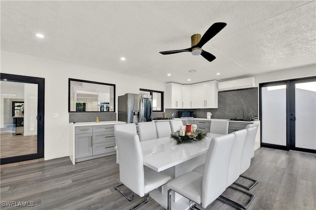 dining space featuring a wall mounted air conditioner, a textured ceiling, light hardwood / wood-style floors, and ceiling fan