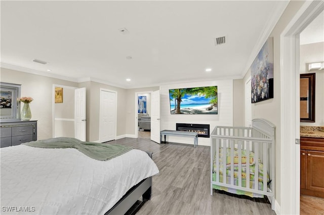 bedroom with light wood-type flooring, ensuite bath, a closet, and crown molding