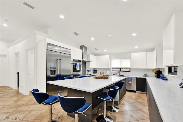 kitchen featuring a kitchen bar, appliances with stainless steel finishes, ventilation hood, white cabinets, and a kitchen island