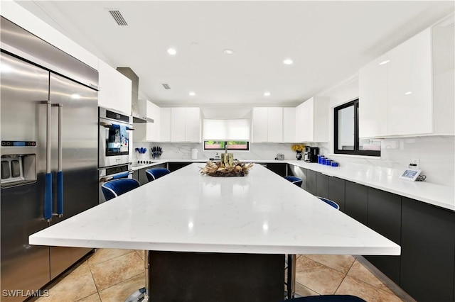 kitchen with light stone countertops, a kitchen island, a kitchen bar, white cabinetry, and stainless steel appliances