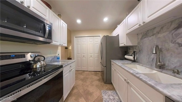 kitchen with appliances with stainless steel finishes, tasteful backsplash, sink, light tile patterned floors, and white cabinetry