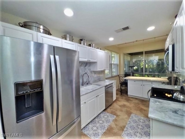 kitchen featuring white cabinetry, sink, tasteful backsplash, light stone counters, and appliances with stainless steel finishes