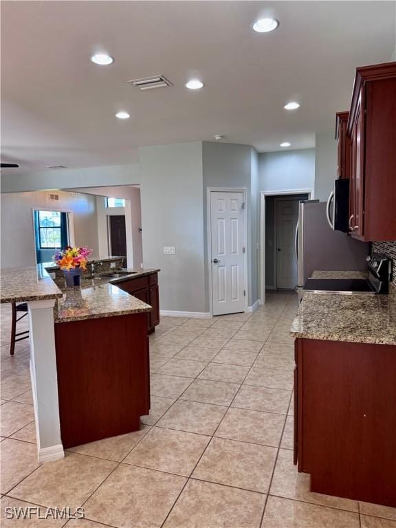 kitchen featuring a center island, light stone countertops, light tile patterned flooring, a kitchen bar, and stainless steel appliances