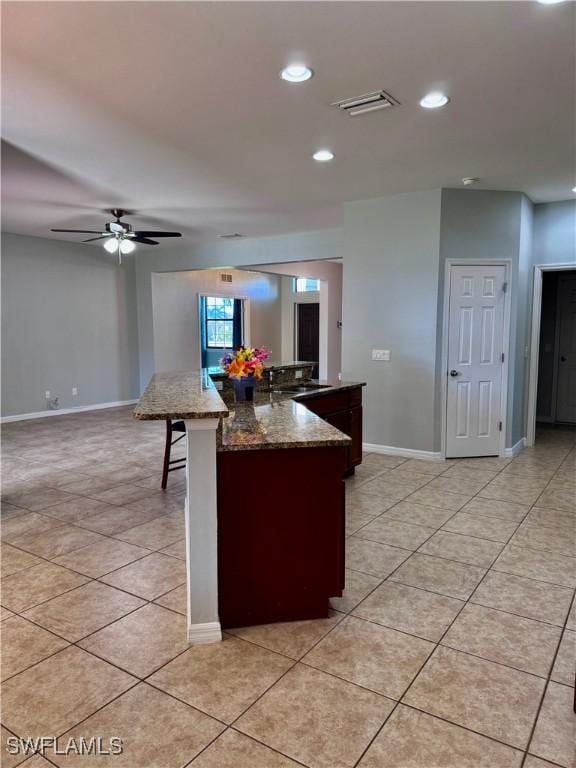 kitchen featuring ceiling fan, a kitchen breakfast bar, light stone counters, a center island with sink, and light tile patterned flooring