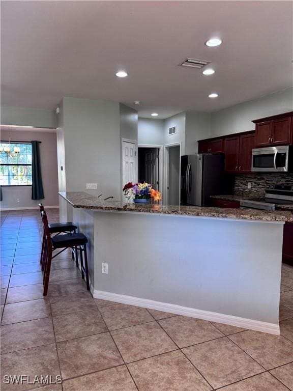 kitchen featuring stone countertops, decorative backsplash, light tile patterned floors, appliances with stainless steel finishes, and a notable chandelier