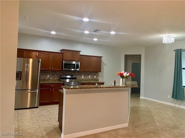 kitchen with decorative backsplash, dark stone countertops, a kitchen island with sink, and appliances with stainless steel finishes