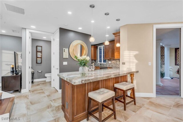 kitchen with kitchen peninsula, light stone countertops, backsplash, a breakfast bar, and pendant lighting