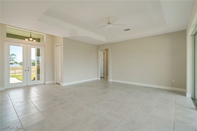 tiled spare room with a raised ceiling, french doors, and ceiling fan with notable chandelier