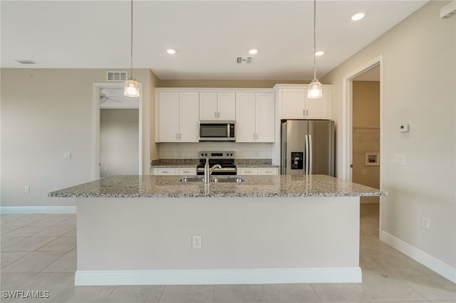 kitchen featuring an island with sink, white cabinets, stainless steel appliances, and light stone counters