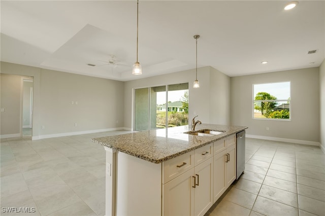 kitchen featuring a center island with sink, ceiling fan, light stone countertops, a tray ceiling, and white cabinetry