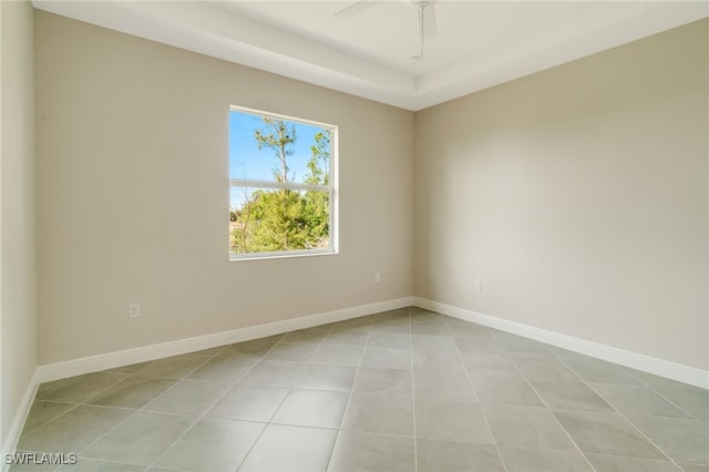 tiled empty room with ceiling fan and a tray ceiling