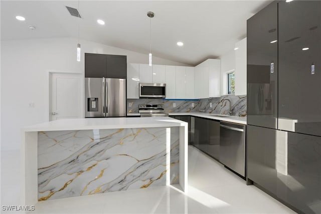 kitchen featuring pendant lighting, lofted ceiling, decorative backsplash, white cabinets, and appliances with stainless steel finishes