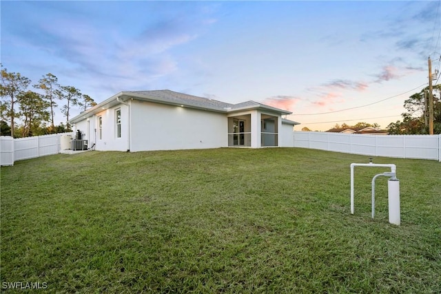 back house at dusk featuring cooling unit and a lawn