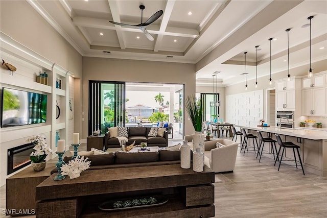 living room featuring light wood-type flooring, coffered ceiling, ceiling fan, sink, and beamed ceiling