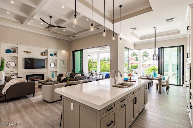 kitchen with coffered ceiling, a center island with sink, sink, decorative light fixtures, and light hardwood / wood-style floors