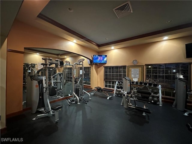 gym featuring a raised ceiling and crown molding