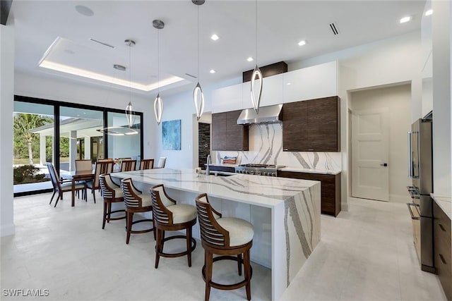 kitchen featuring dark brown cabinetry, white cabinetry, an island with sink, decorative light fixtures, and decorative backsplash