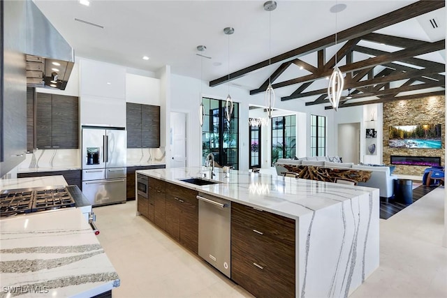 kitchen featuring sink, decorative light fixtures, appliances with stainless steel finishes, a large island, and light stone counters