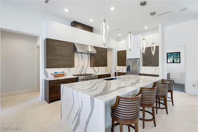 kitchen featuring a center island with sink, wall chimney exhaust hood, pendant lighting, and appliances with stainless steel finishes