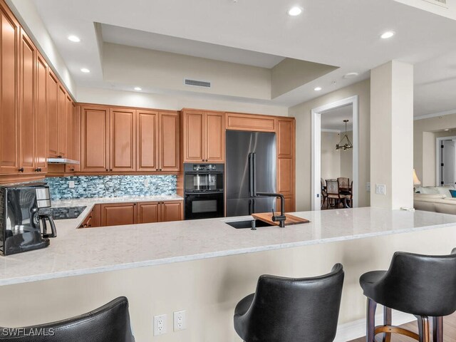 kitchen with black appliances, light stone countertops, a kitchen bar, and kitchen peninsula