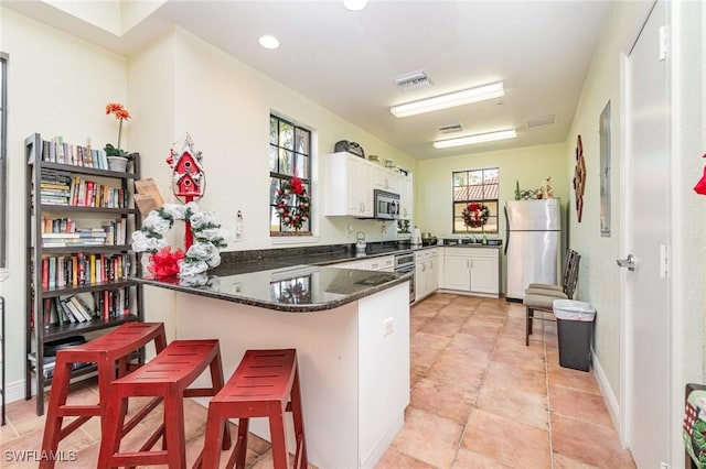 kitchen with dark stone countertops, white cabinetry, a kitchen bar, kitchen peninsula, and stainless steel appliances