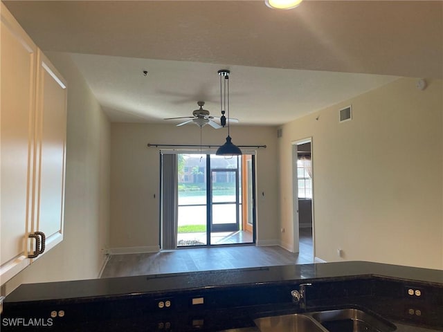 kitchen with a sink, visible vents, baseboards, a ceiling fan, and dark countertops