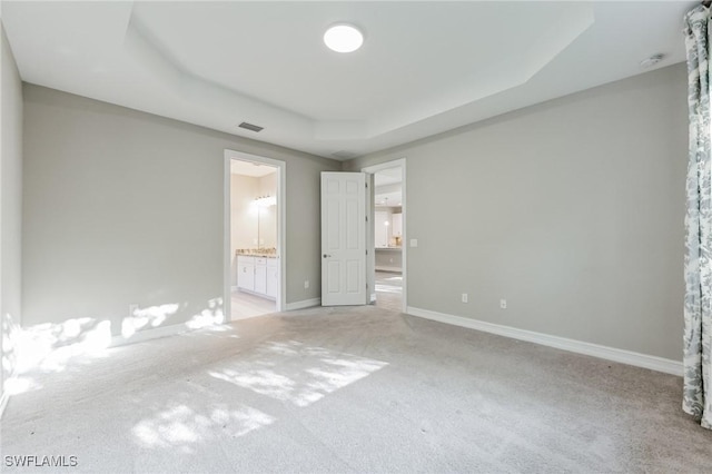 unfurnished bedroom with light carpet, a tray ceiling, and ensuite bath