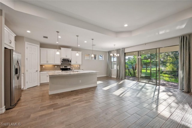 kitchen with appliances with stainless steel finishes, a kitchen island with sink, pendant lighting, white cabinets, and a chandelier