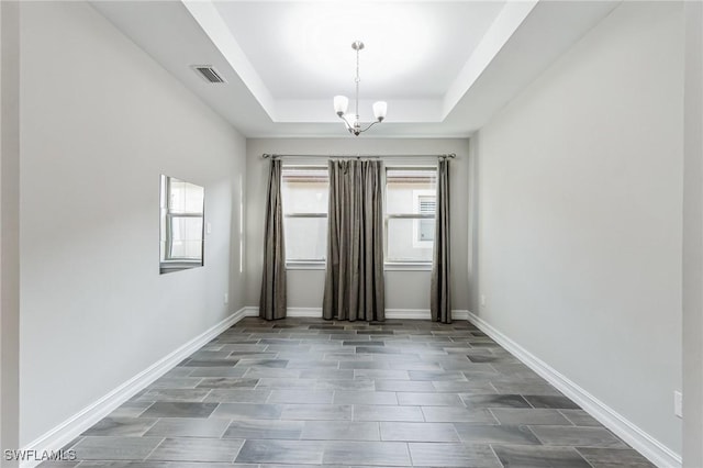 spare room featuring a raised ceiling and a chandelier