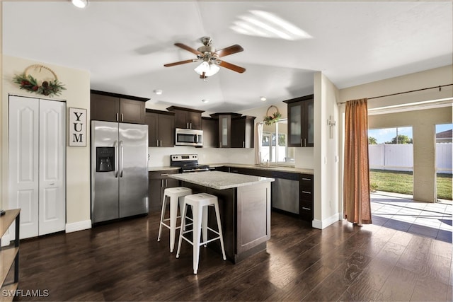 kitchen with dark wood-type flooring, a breakfast bar area, a center island, dark brown cabinets, and appliances with stainless steel finishes