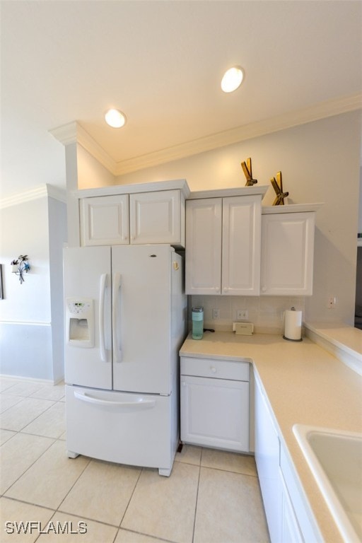 kitchen with white refrigerator with ice dispenser, light tile patterned floors, white cabinets, and ornamental molding