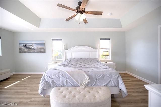 bedroom featuring a raised ceiling, multiple windows, and light hardwood / wood-style floors