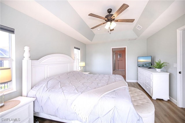 bedroom featuring ceiling fan, a raised ceiling, wood-type flooring, and multiple windows