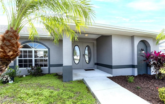 entrance to property featuring french doors, a lawn, and stucco siding