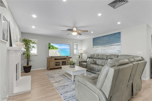 living room featuring a fireplace, light wood-type flooring, and ceiling fan