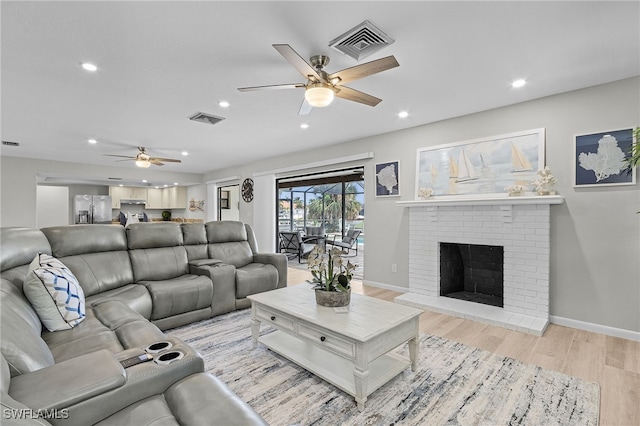 living room featuring ceiling fan, light hardwood / wood-style floors, and a brick fireplace