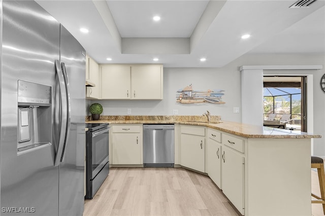 kitchen featuring a tray ceiling, kitchen peninsula, cream cabinets, and appliances with stainless steel finishes