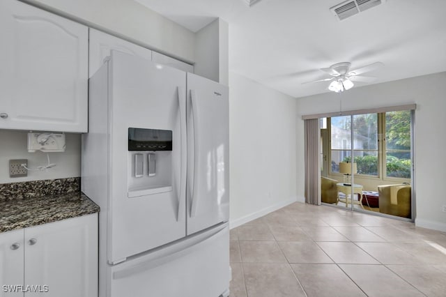 kitchen featuring white cabinetry, ceiling fan, white refrigerator with ice dispenser, dark stone countertops, and light tile patterned floors