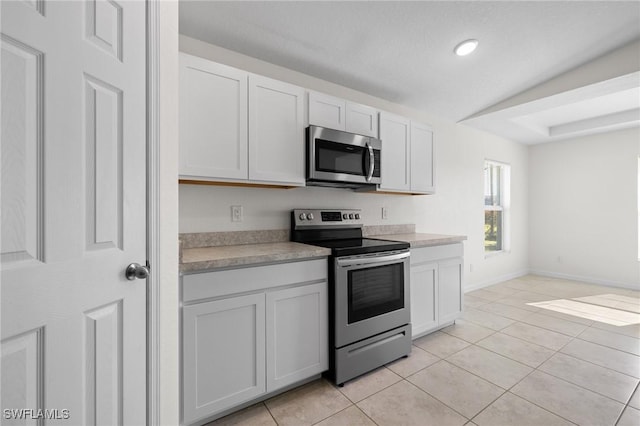 kitchen with appliances with stainless steel finishes, white cabinetry, lofted ceiling, and light tile patterned flooring