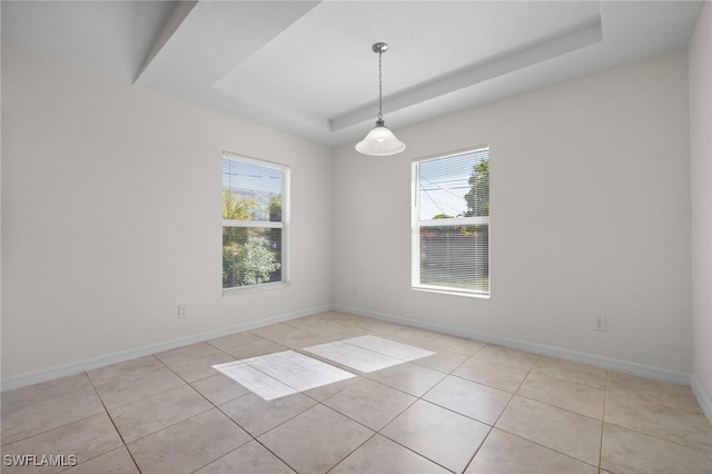 unfurnished room with a tray ceiling, a wealth of natural light, and light tile patterned flooring