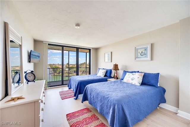 bedroom featuring access to exterior, floor to ceiling windows, light wood-style floors, and baseboards