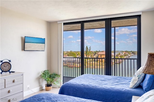 bedroom with access to outside, floor to ceiling windows, a water view, and baseboards