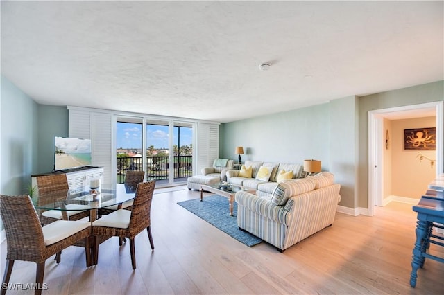 living room featuring expansive windows, light wood-style flooring, baseboards, and a textured ceiling