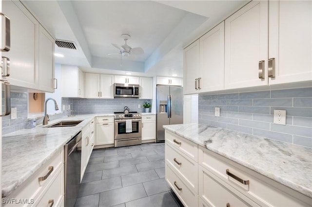 kitchen with a sink, stainless steel appliances, a raised ceiling, and white cabinetry