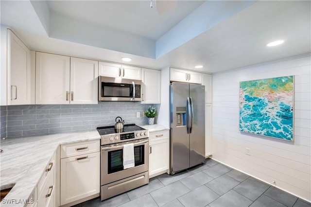 kitchen featuring stainless steel appliances, white cabinets, decorative backsplash, and light stone countertops