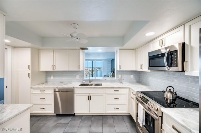 kitchen featuring a sink, a ceiling fan, white cabinets, appliances with stainless steel finishes, and light stone countertops