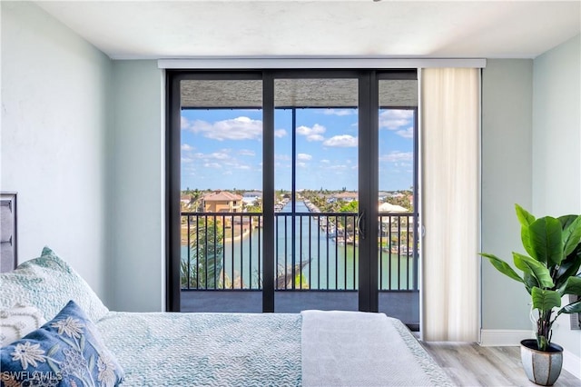 bedroom with a water view, wood finished floors, baseboards, access to outside, and a wall of windows