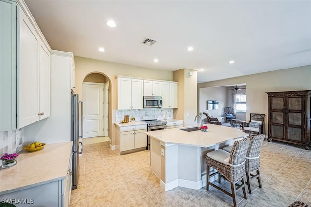 kitchen featuring decorative backsplash, stainless steel appliances, a kitchen island with sink, sink, and white cabinetry