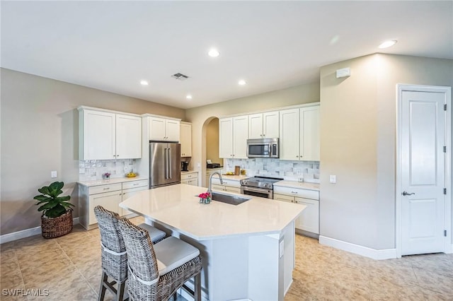 kitchen featuring decorative backsplash, appliances with stainless steel finishes, sink, white cabinets, and an island with sink